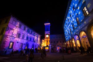 A gobo projection of a Christmas tree against a city building washed in purple light is a beautiful example of holiday light displays for public spaces.